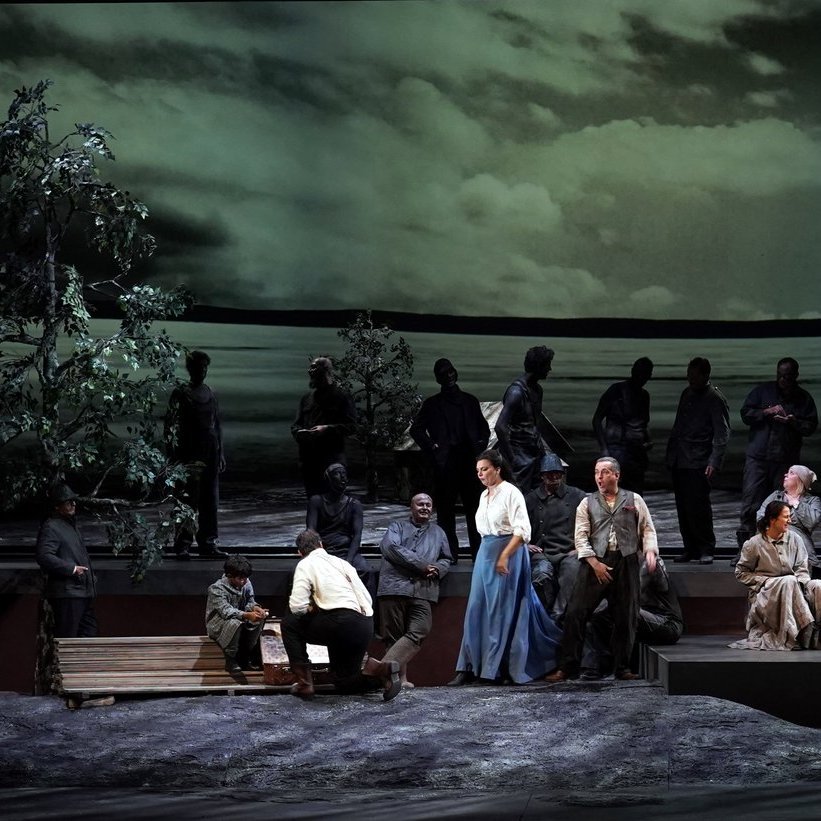 Aufführung der Oper Sibirien, viele verschiedene Leute sind auf der Bühne, sie sitzen an Tischen oder stehen da