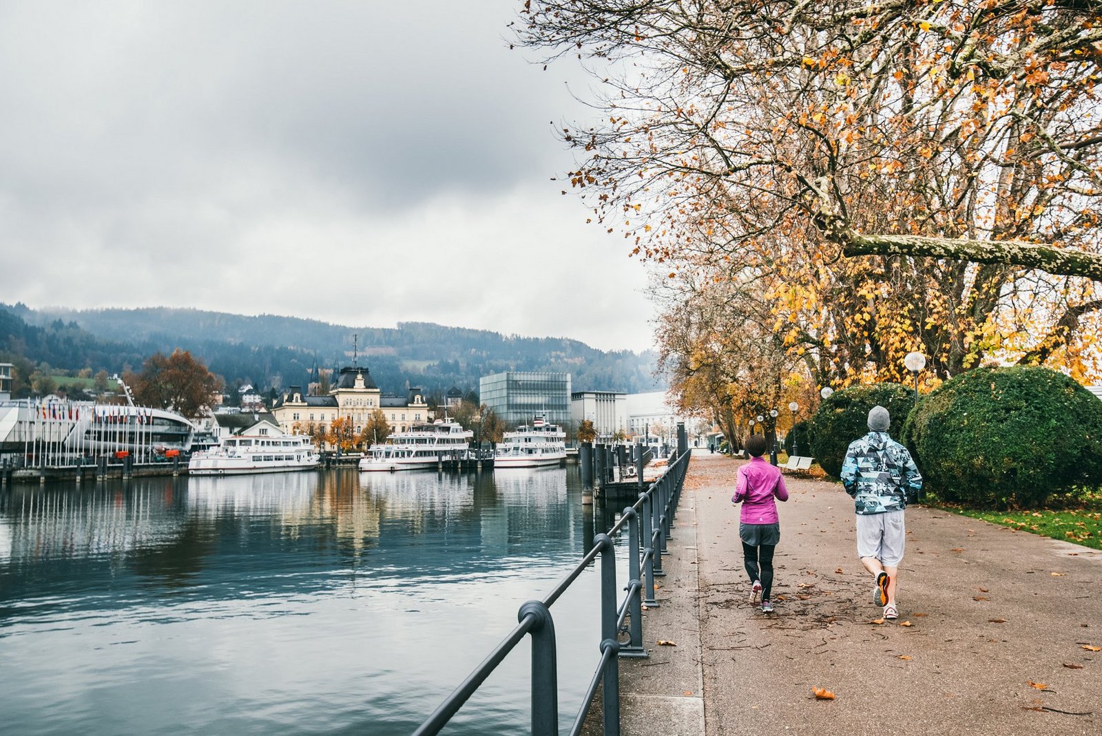 Zwei Läufer laufen entlang des herbstlichen Bregenzer Hafens in Richtung Stadt