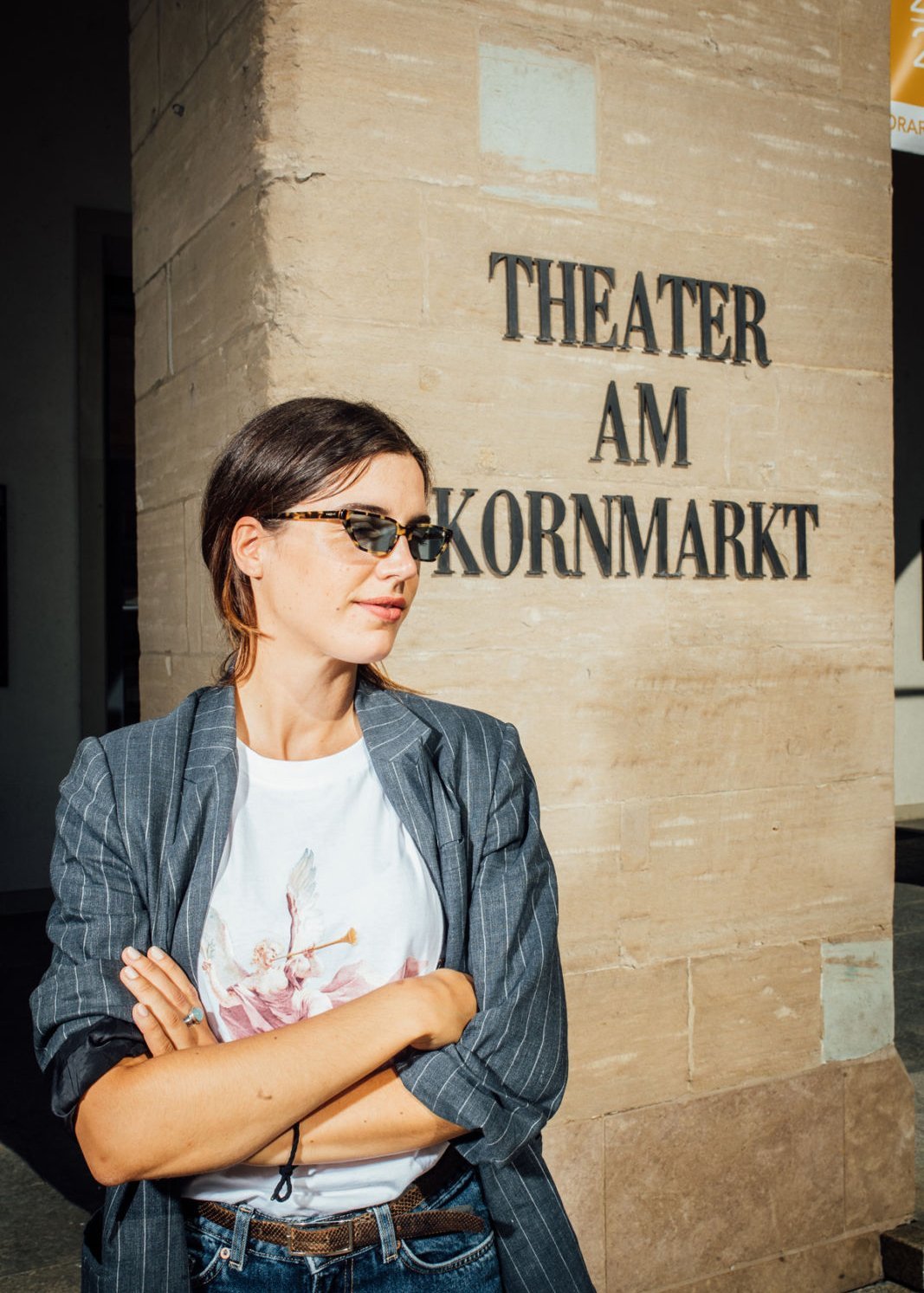 Eine junge Frau mit Sonnenbrille steht vor dem Schriftzug des Theaters am Kornmarkt