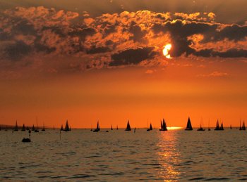 Blick auf den Sonnenuntergang mit der Silhouette von vielen Segelschiffen 
