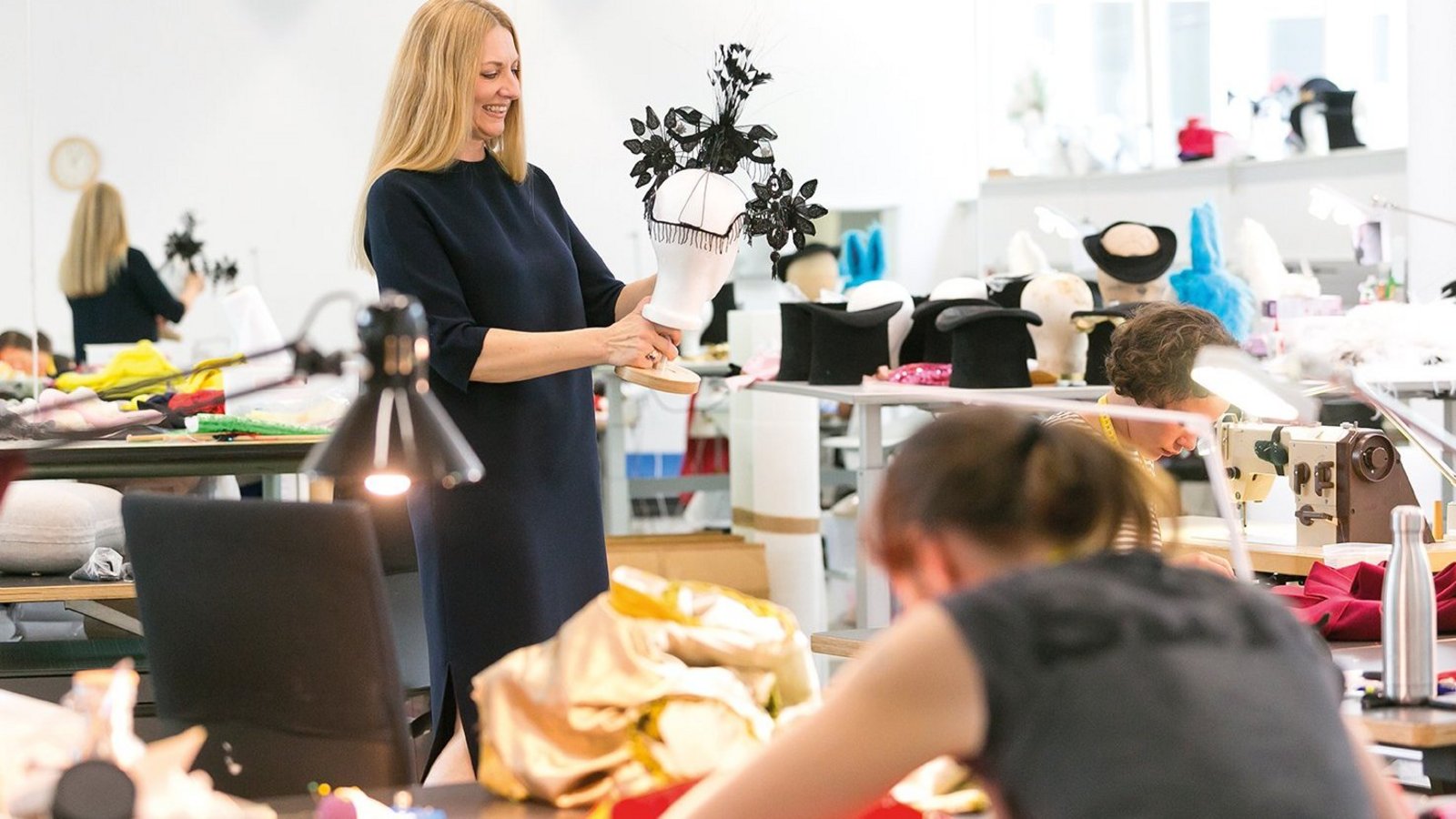 Eine Frau, in einem Atelier stehend, hält eine Auswahl an Kleidern