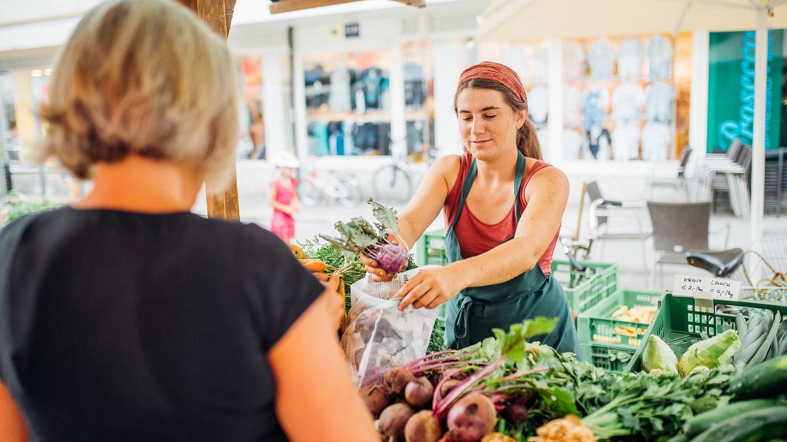 Eine Verkäuferin überreicht der Kundin frisches Gemüse am Marktstand