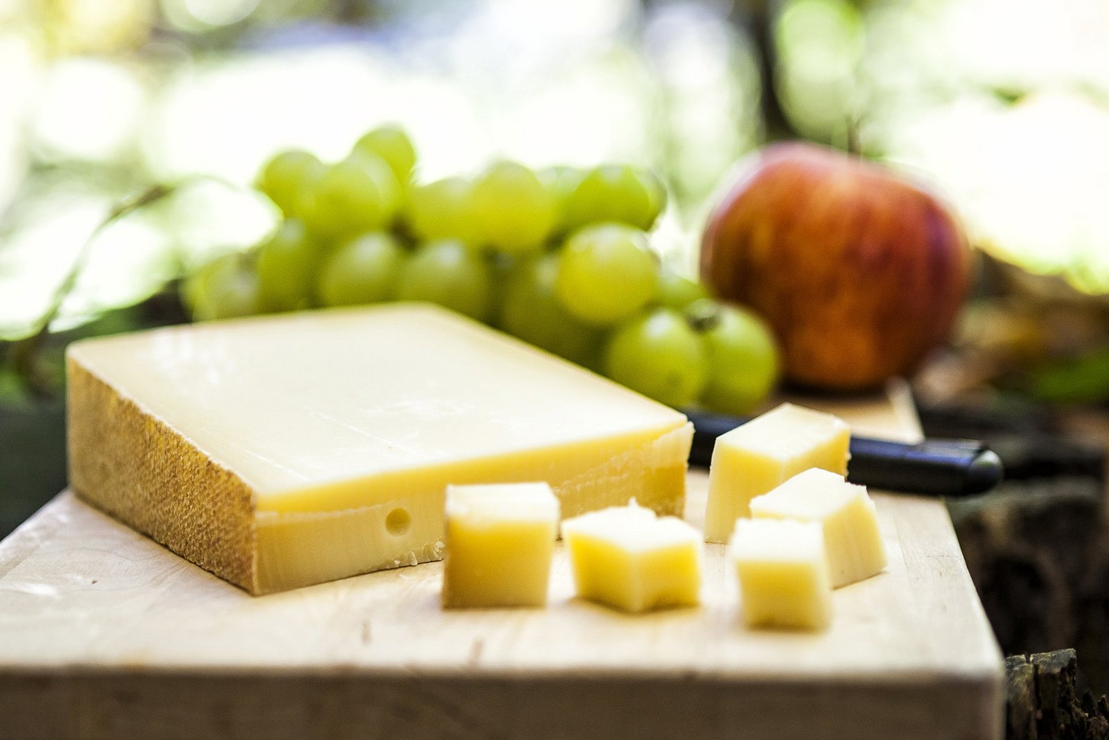Bild von Käse, im Hintergrund Trauben und Äpfel