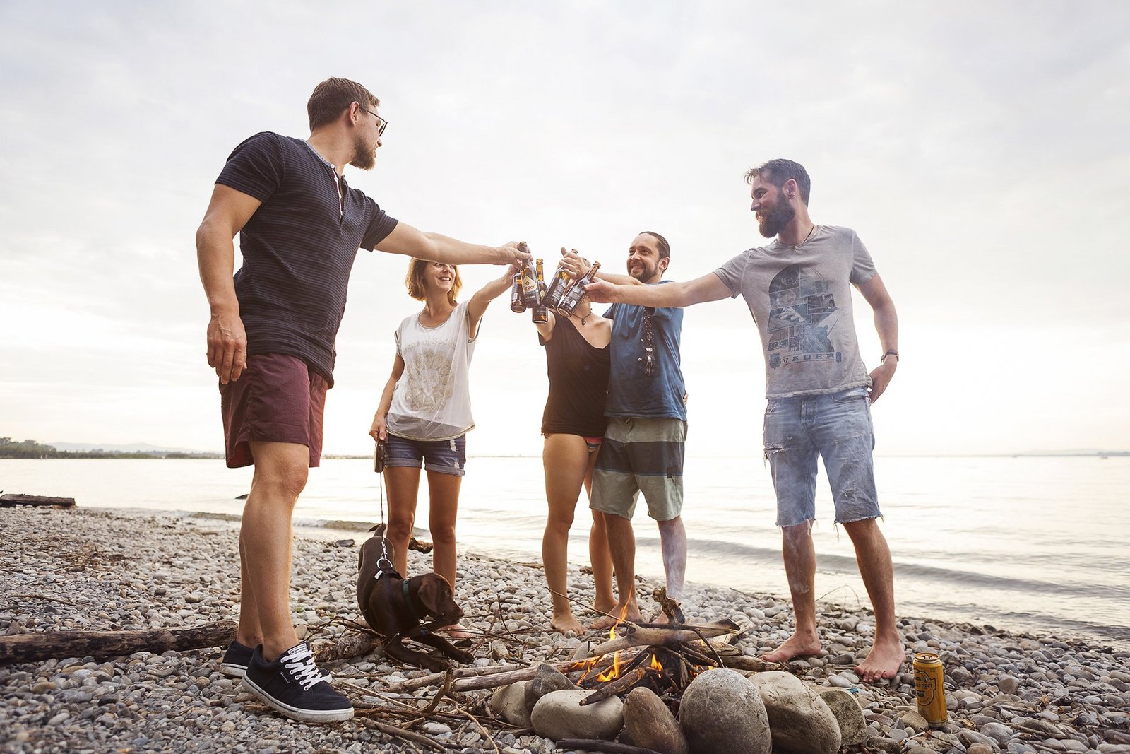 Eine Gruppe junger Menschen stoßt mit einem Bier am Strand von Neu-Amerika an