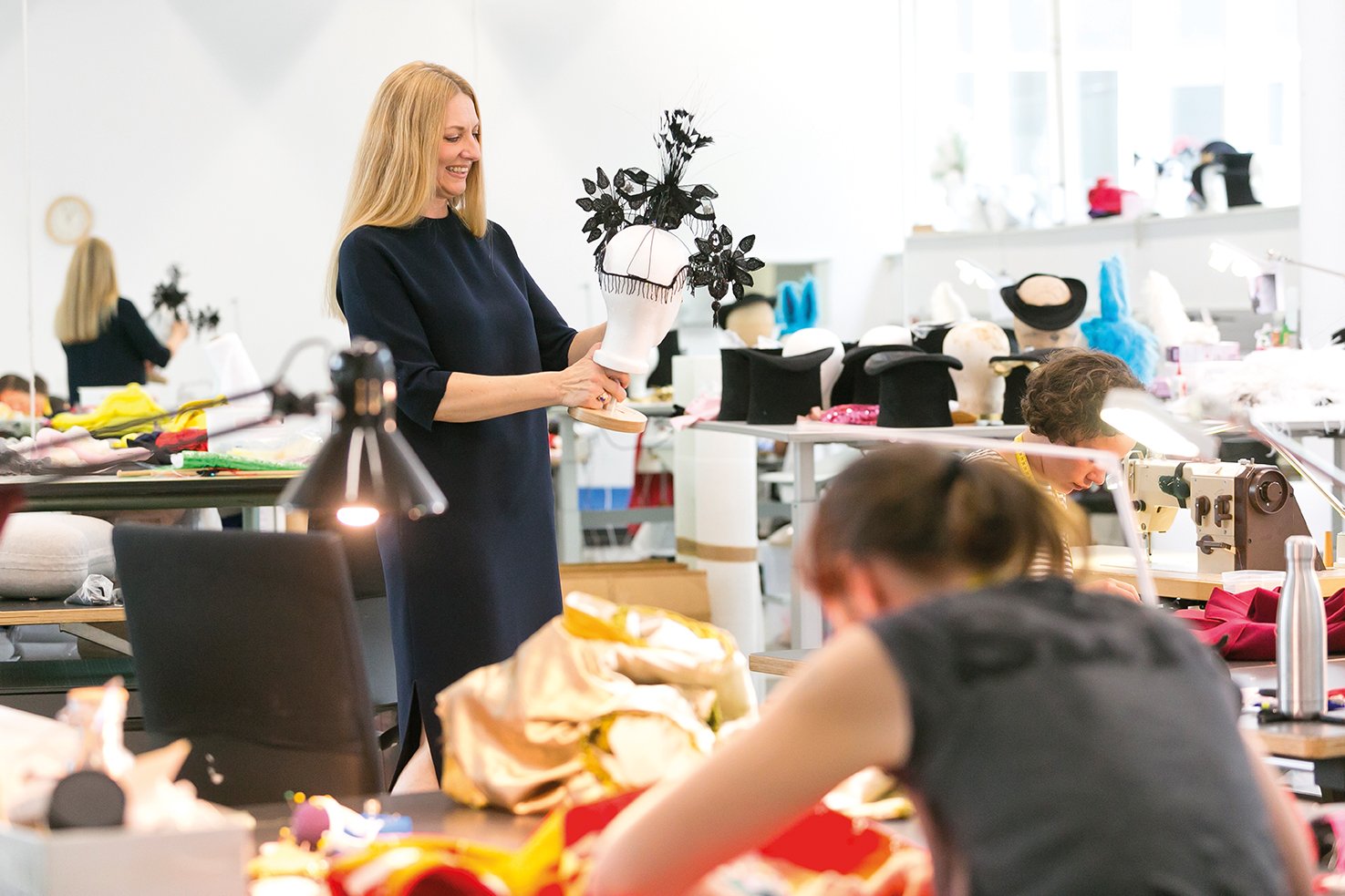 Eine Frau, in einem Atelier stehend, hält eine Auswahl an Kleidern