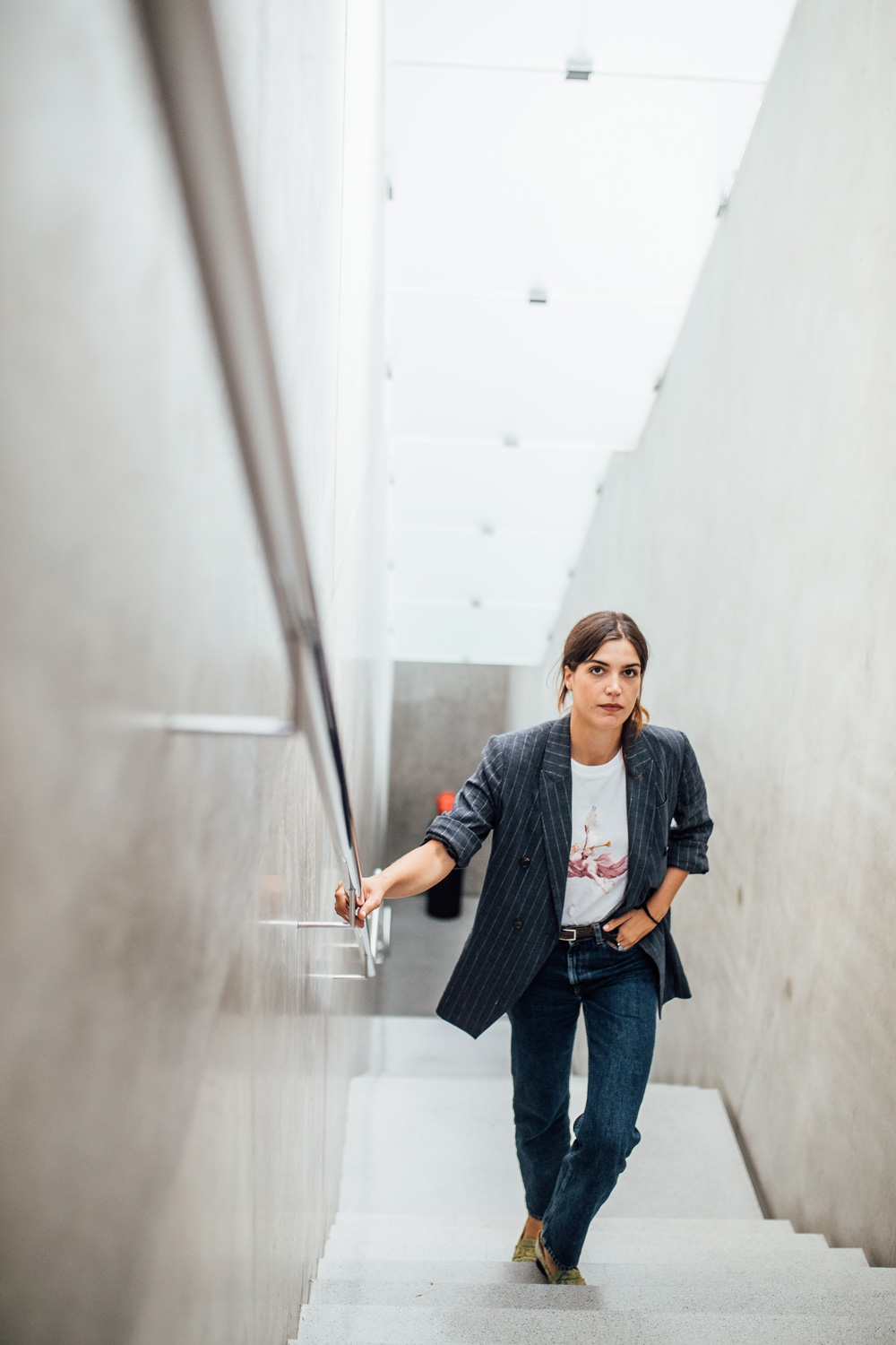 Eine junge Dame steigt die Treppen des Kunsthauses Bregenz nach oben und lächelt in die Kamera