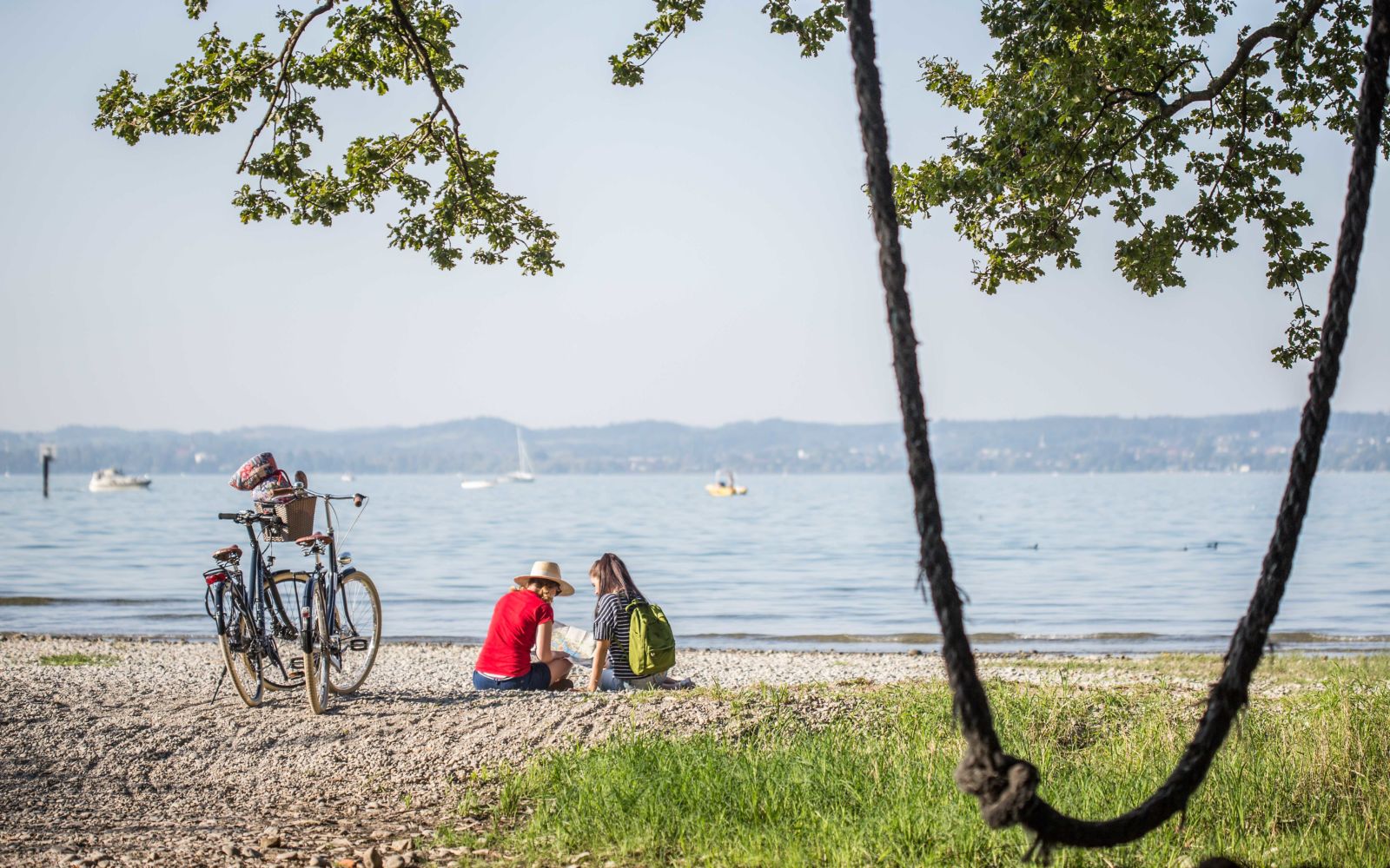 Zwei Frauen sitzen am Bodensee daneben stehen zwei Fahrräder