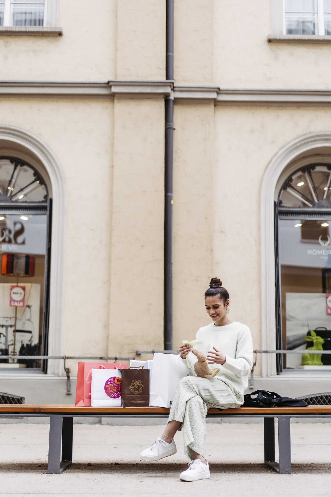Eine Frau mit Einkaufstaschen sitzt auf einer Bank in Bregenz